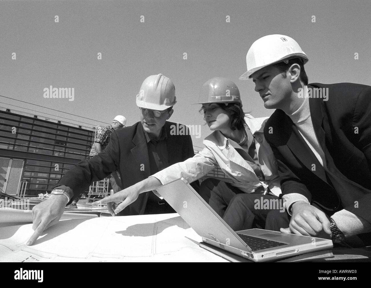 Three people with hard hats examining blueprints, b&w Stock Photo