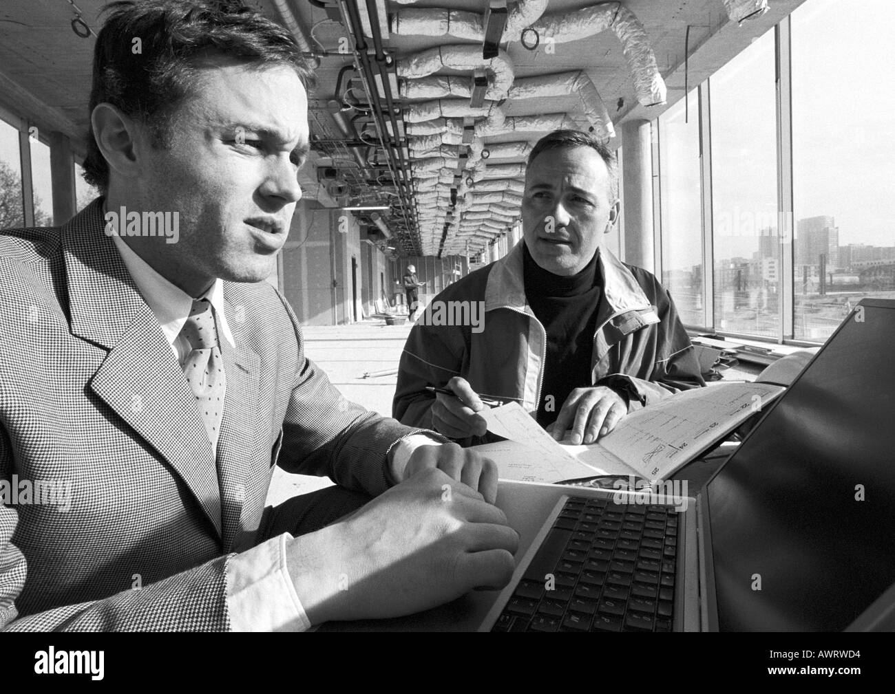 Man looking at agenda, second man using laptop computer, b&w Stock Photo