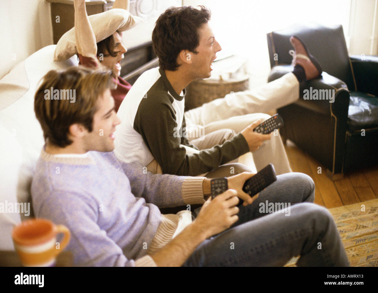Three men sitting on sofa with remote controls, side view Stock Photo
