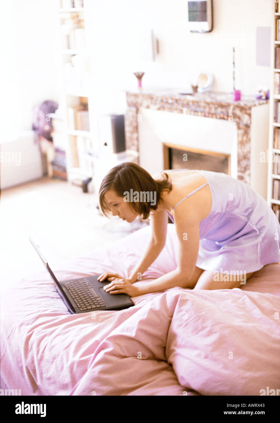 Woman kneeling on bed, using laptop computer Stock Photo