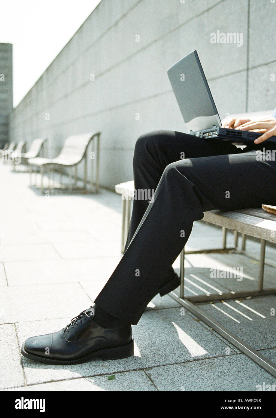 Man on bench with laptop computer on knees, close-up Stock Photo
