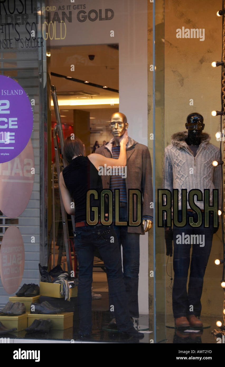 Young woman dressing a gold mannequin in a men's clothes shop  window Stock Photo