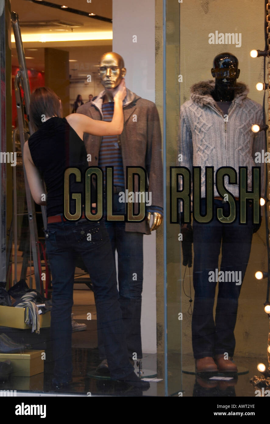 Young woman dressing  a golden mannequin in a men's clothes shop window. Stock Photo