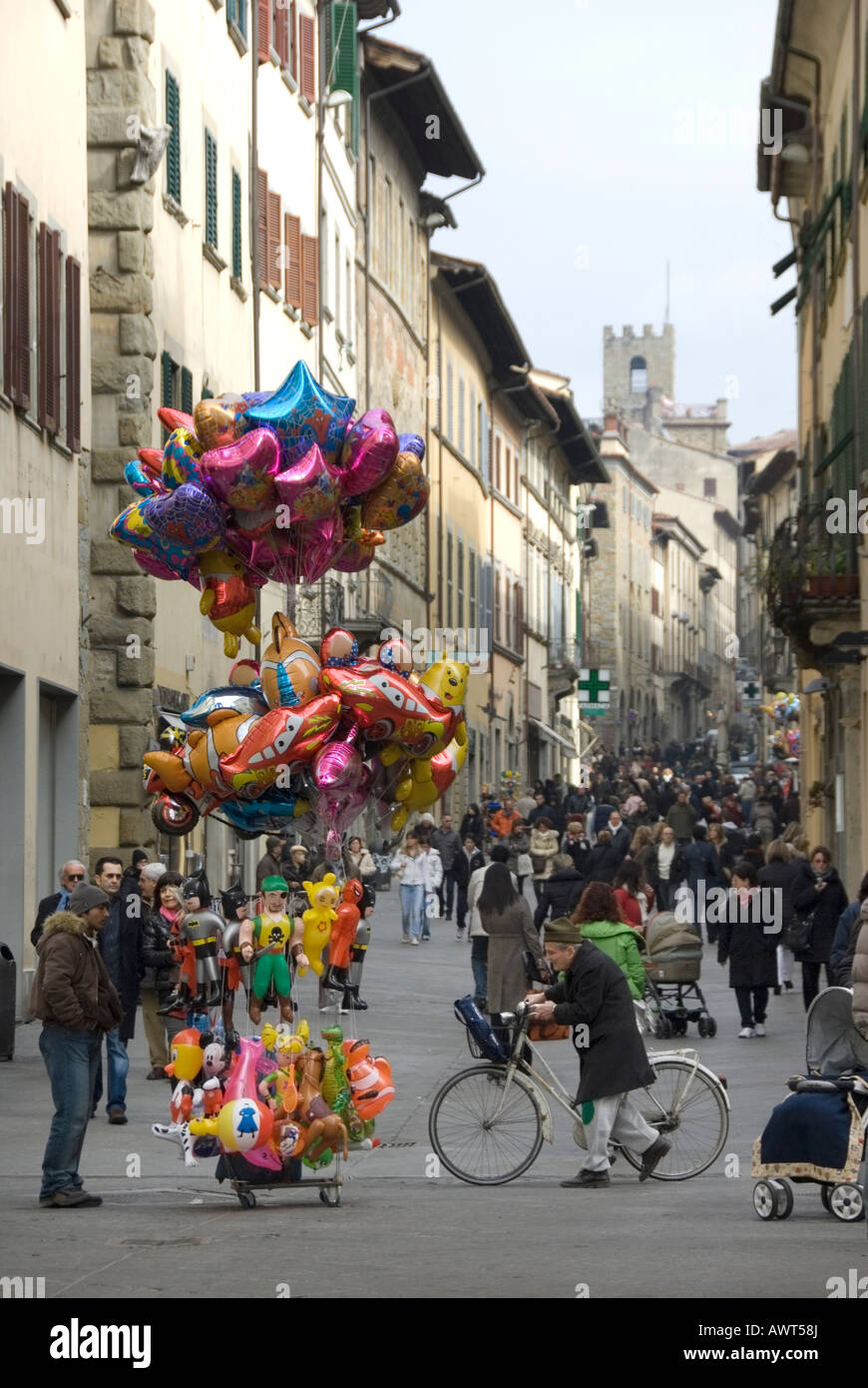 Balloon seller and old man wheels a bicycle across the evening passeggiata in Corso Italia the main shopping street of Arezzo Stock Photo
