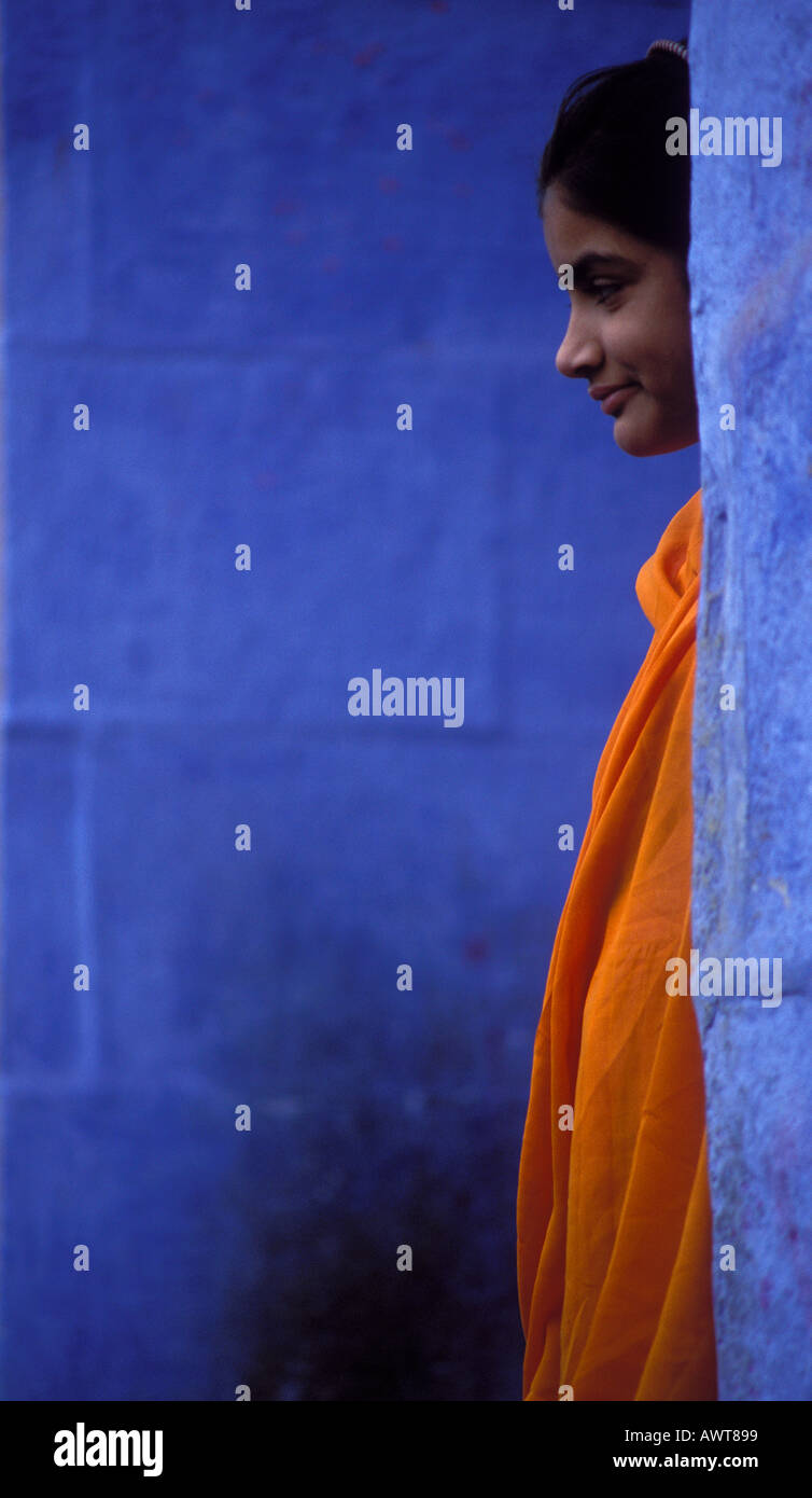 Young women wearing orange Sari stands between blue walls Jodhpur Rajasthan India Stock Photo