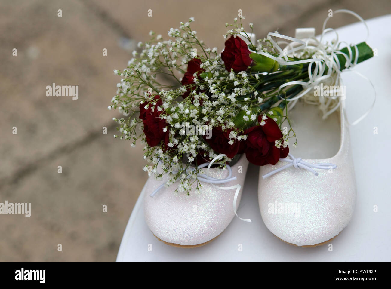 A pair of a child's briesmade shoes and a bouquet roses on a table following a wedding. Stock Photo