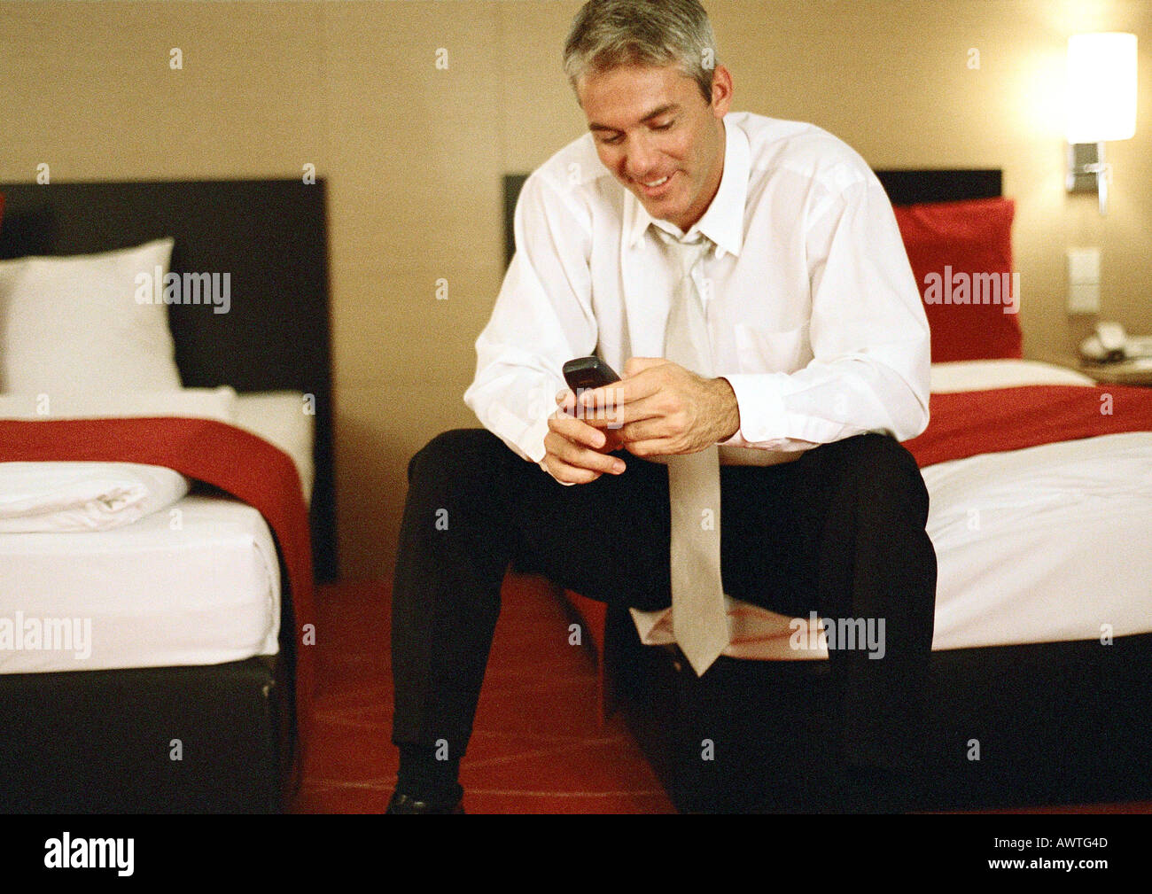 Businessman sitting on bed, using cell phone Stock Photo