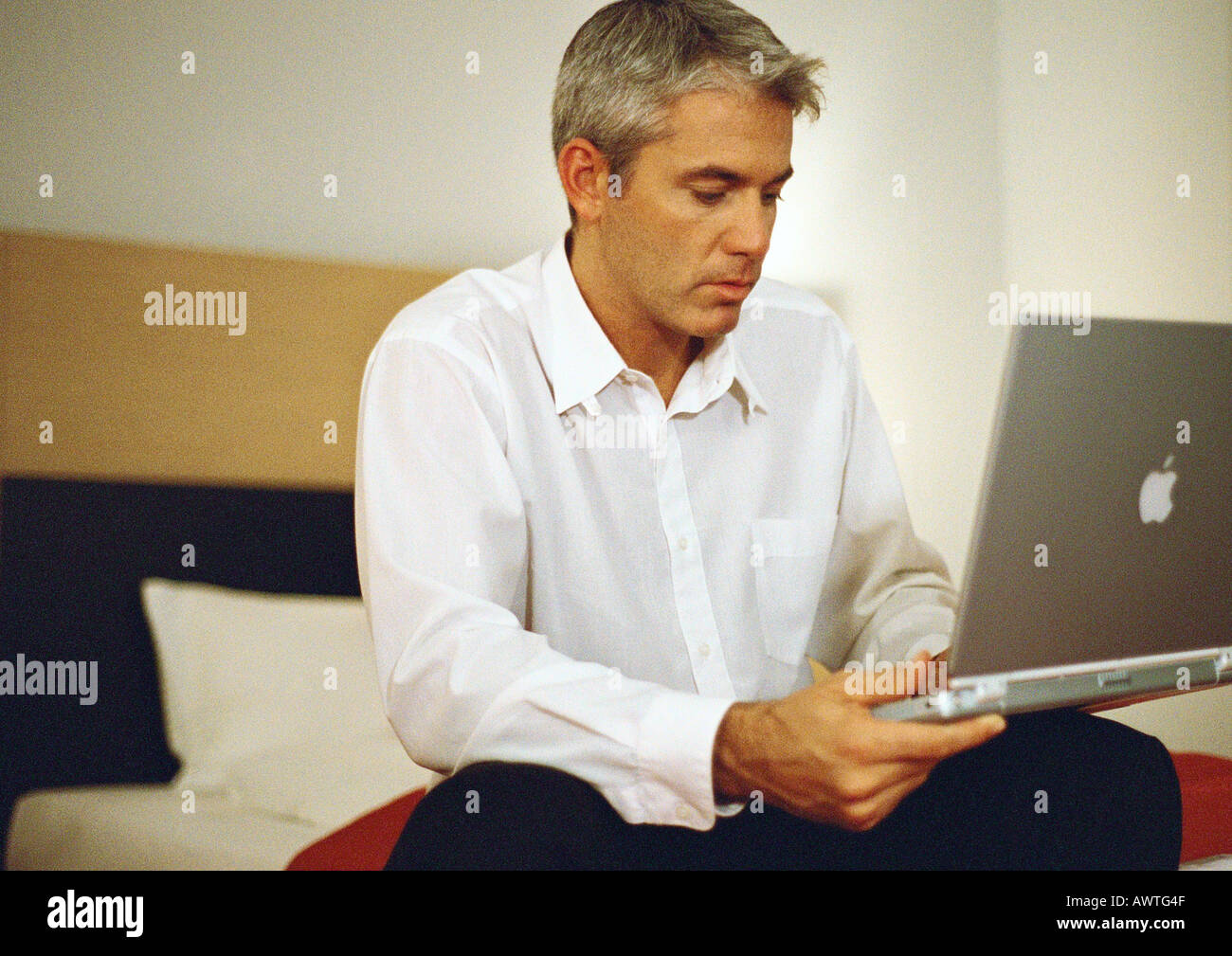 Businessman sitting on bed using laptop Stock Photo