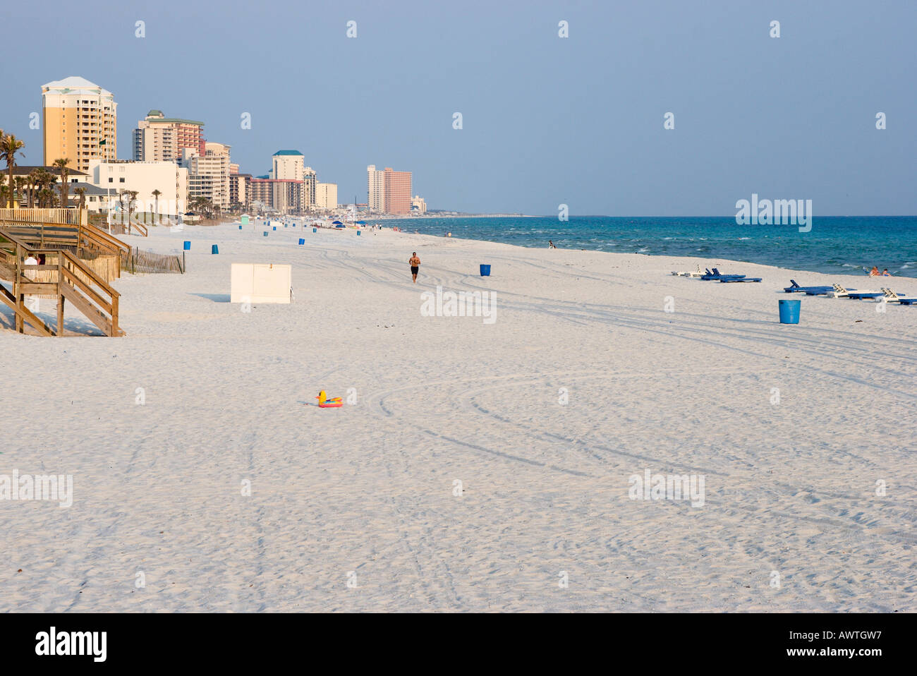 A single jogger jogs along the white sand beach in Florida with the high rise buildings of Panama City Beach in the background Stock Photo