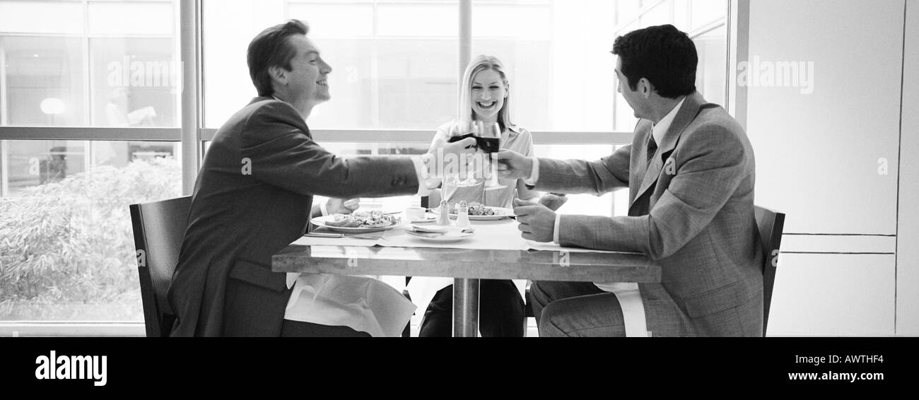 Two businessmen and woman sitting at table clinking glasses, b&w, panoramic view Stock Photo