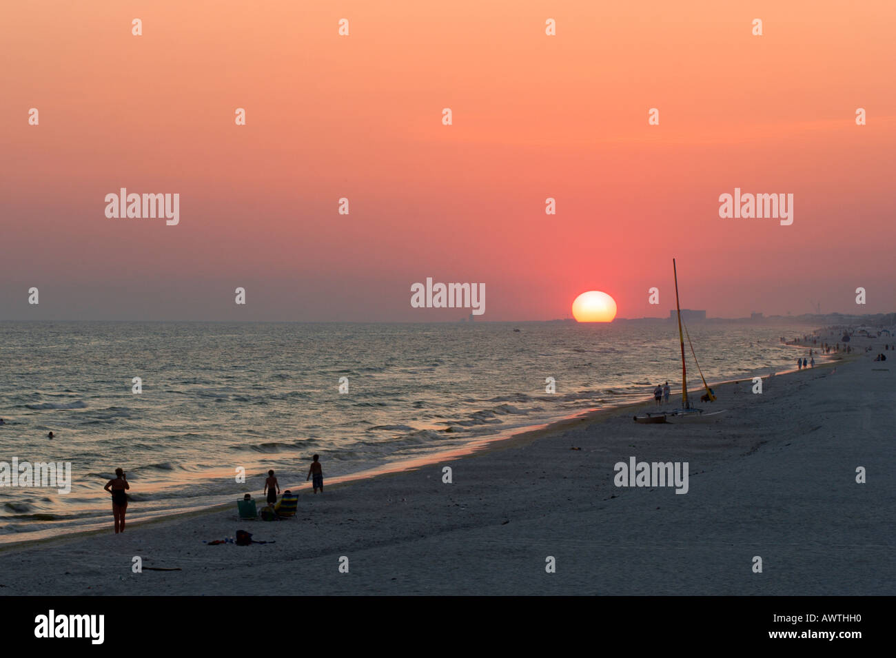 A few people remain on the beach at Panama City Beach Florida after the sun sets with a red glow in the sky Stock Photo