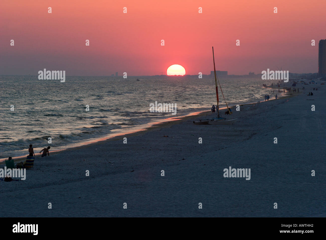A few people remain on the beach at Panama City Beach Florida after the sun sets with a red glow in the sky Stock Photo