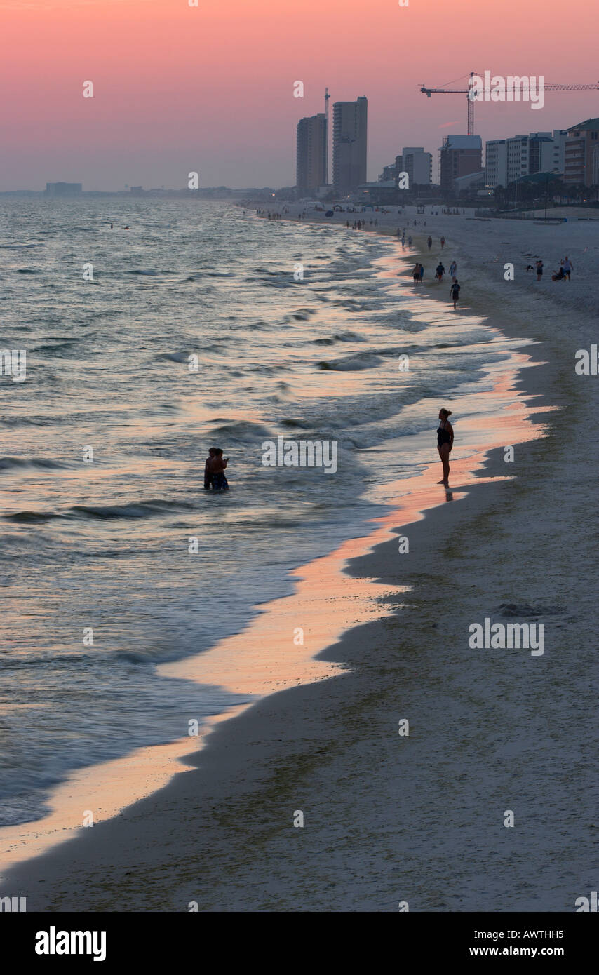 A few people remain on the beach at Panama City Beach Florida after the sun sets with a red glow in the sky Stock Photo