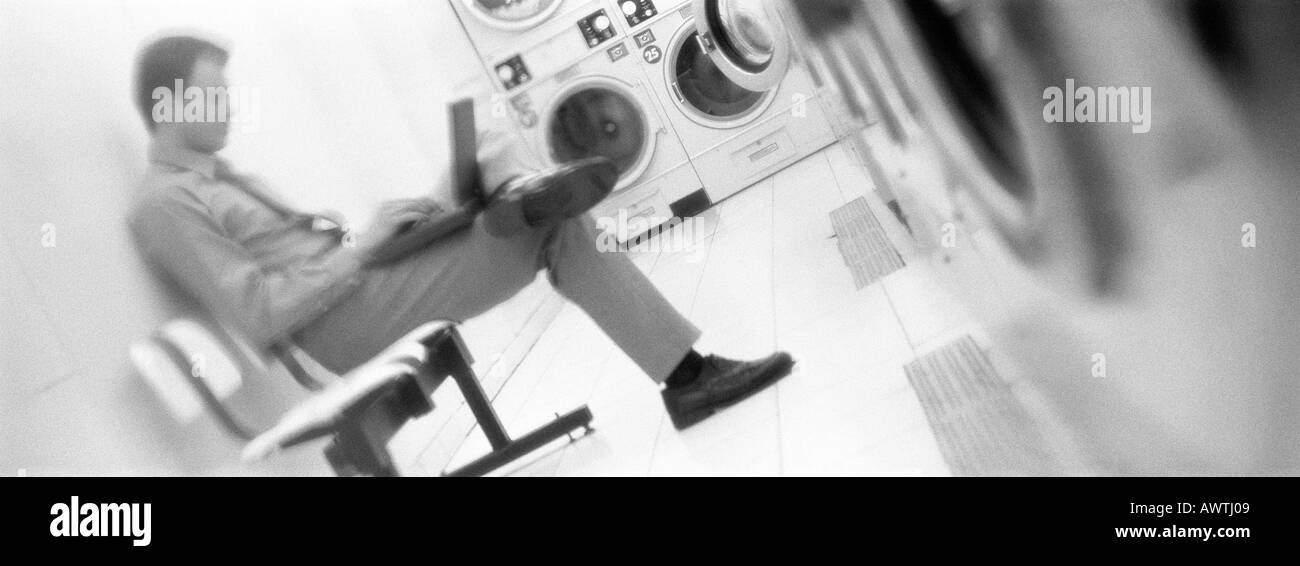 Man sitting and using laptop in laundrymat, b&w, panoramic view Stock Photo
