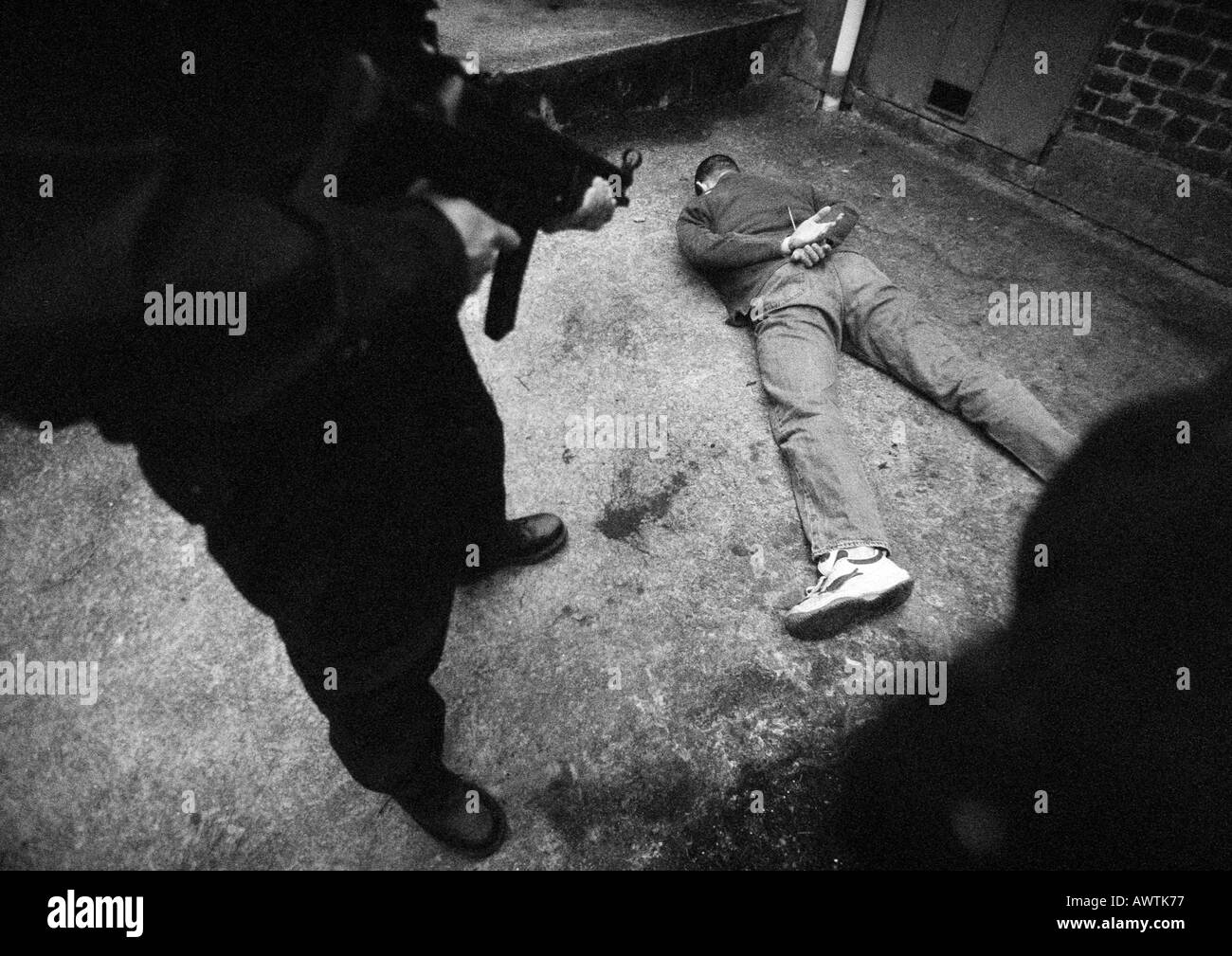 Man standing and pointing sub-machine gun at man face-down on floor, b&w Stock Photo