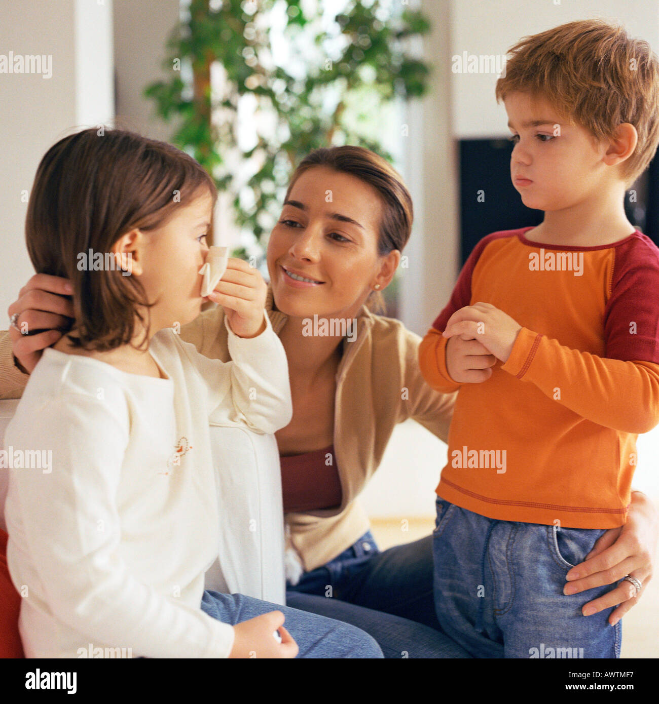 Woman with arms around two children, looking at girl blowing nose Stock Photo