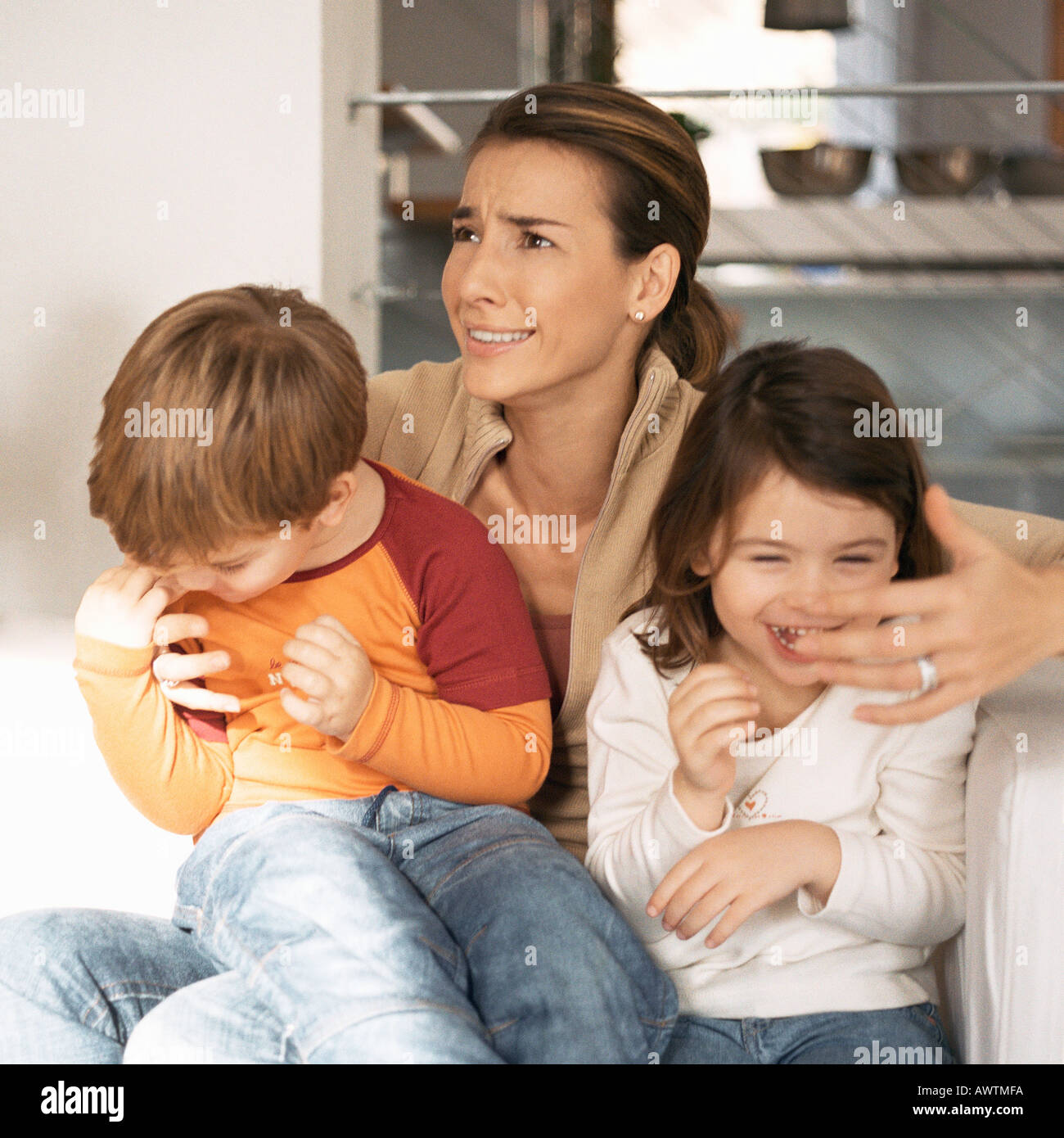 Children sitting on mother's lap, mother making face Stock Photo