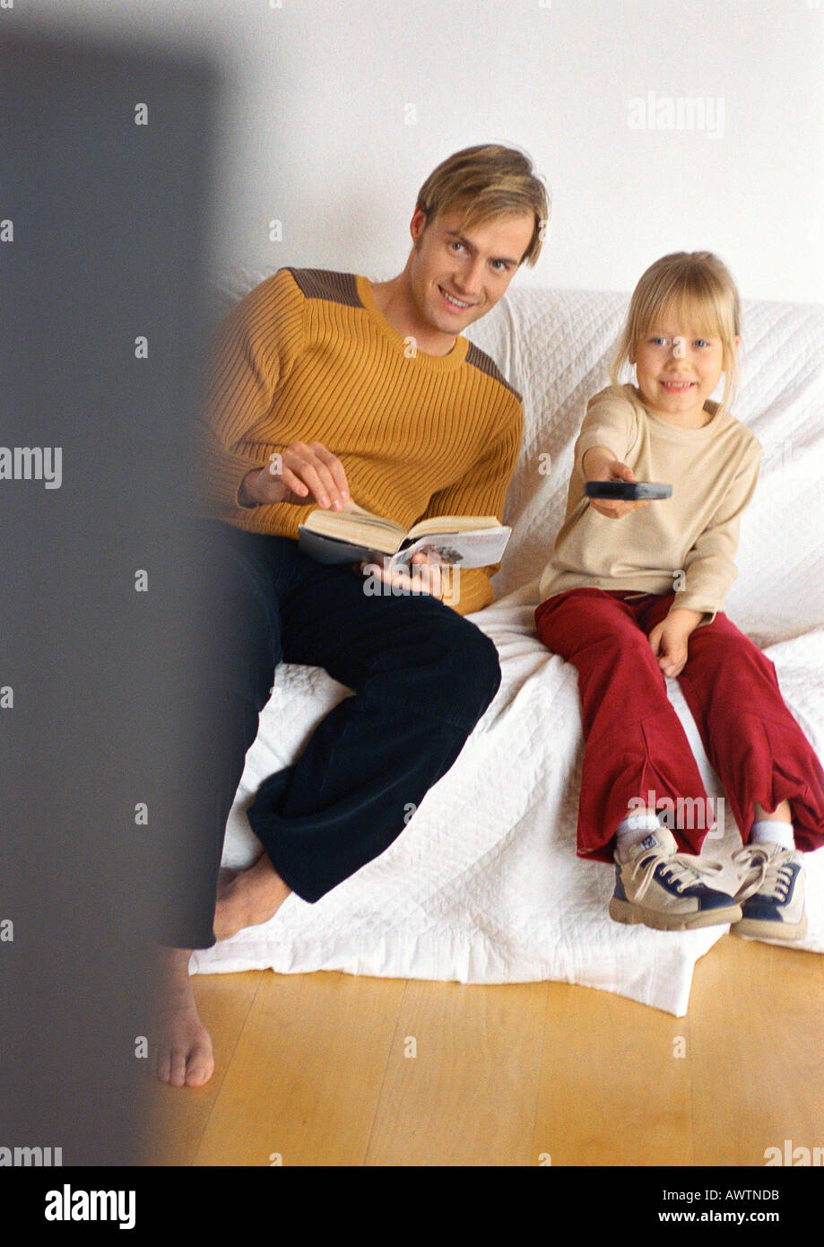 Father sitting next to daughter with remote control. Stock Photo