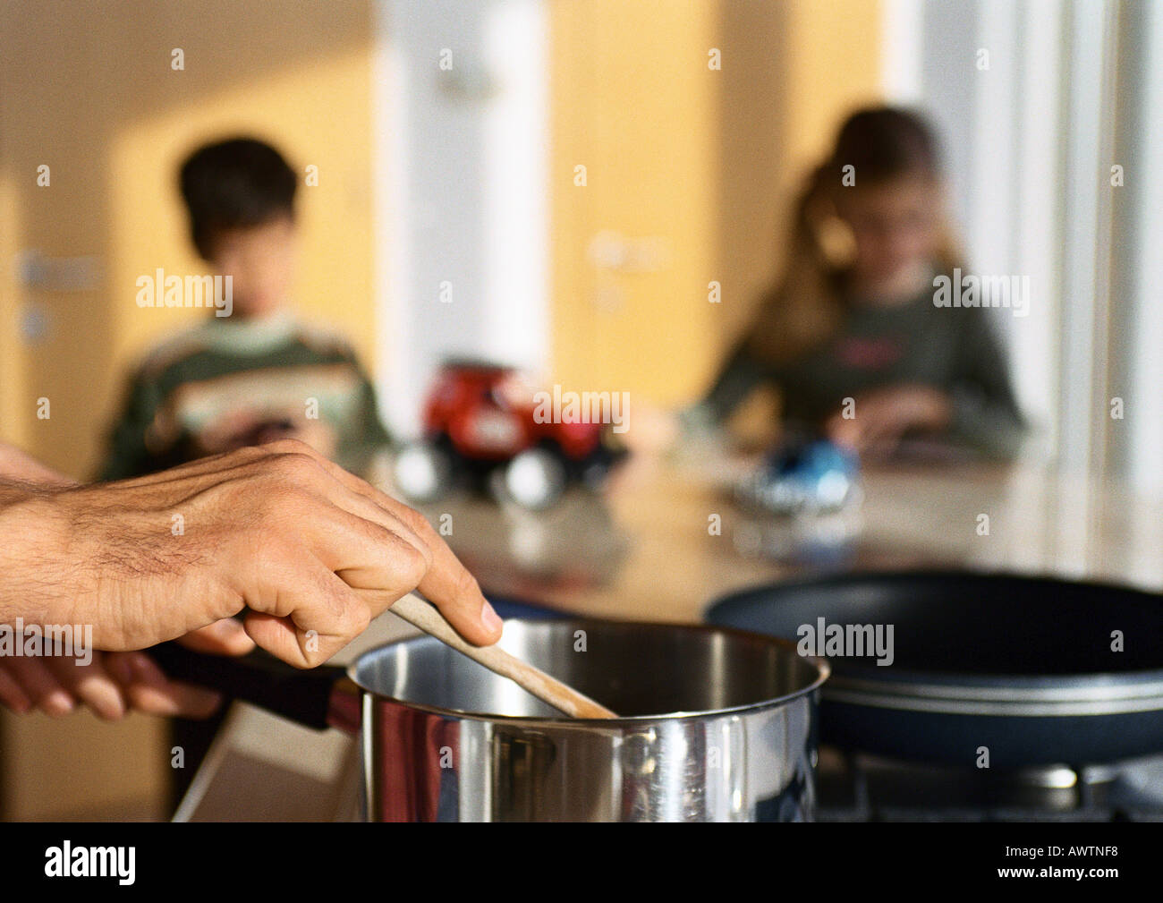 Father cooking in kitchen, children playing at table in background. Stock Photo