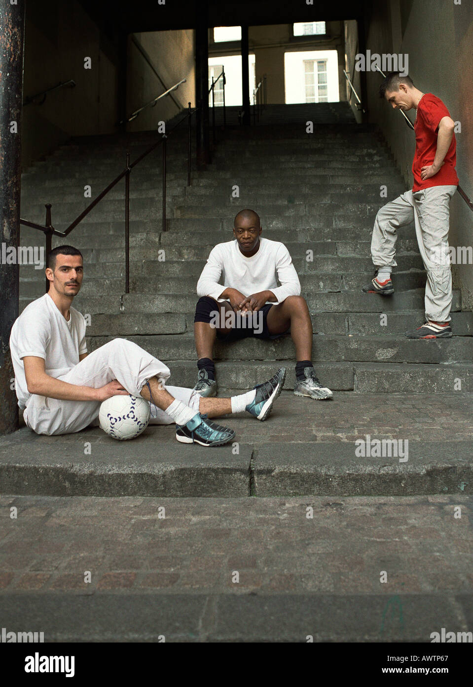Three men sitting on steps with soccer ball Stock Photo