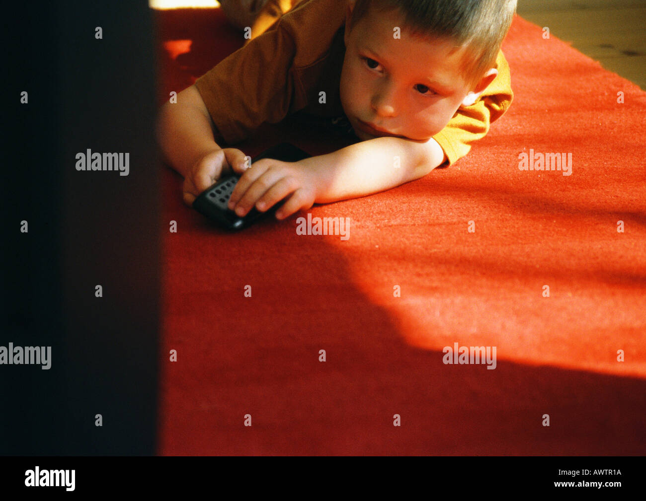 Little boy lying on floor, holding remote control Stock Photo