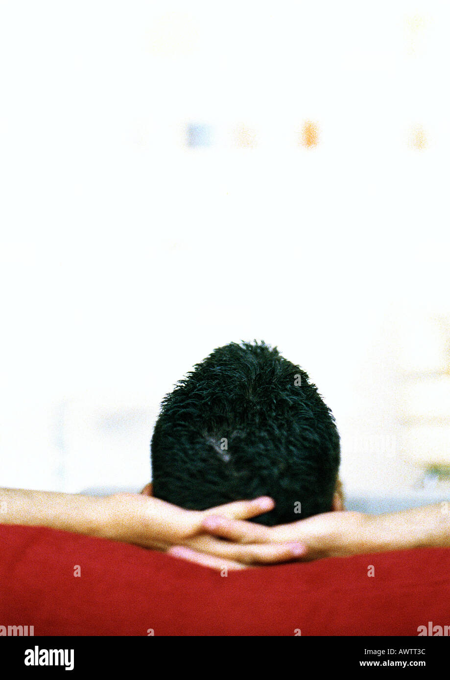 Man sitting with hands behind head, rear view Stock Photo