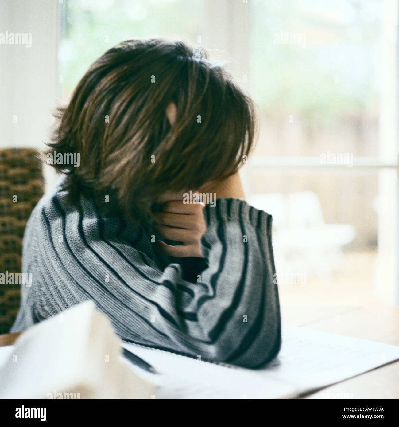 Child leaning on table, looking out window, distracted from doing homework Stock Photo