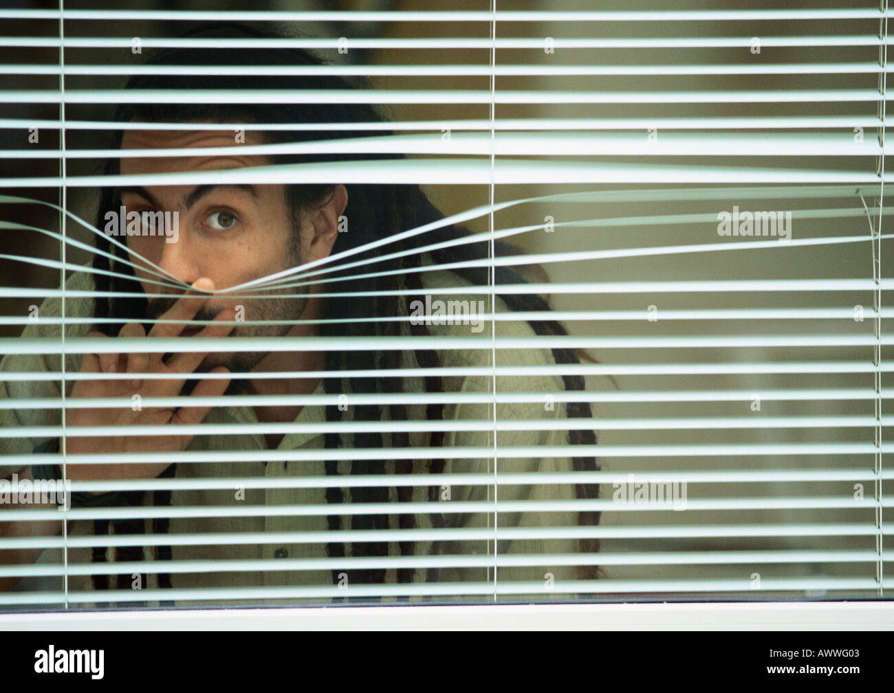 Man looking though blinds Stock Photo