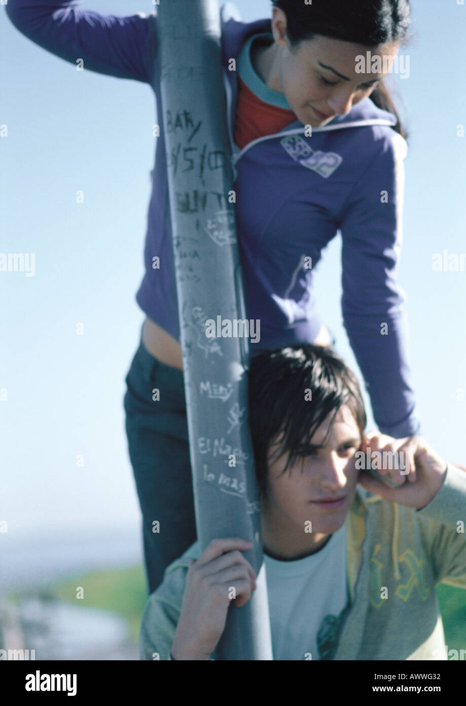 Teenage boy phoning, companion standing on bench behind him playfully leaning on shoulder Stock Photo