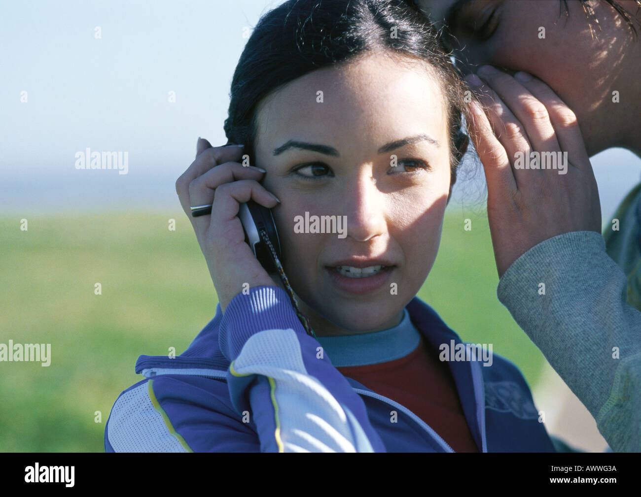 Teenage girl talking on cell phone, friend whispering in her ear, close up Stock Photo
