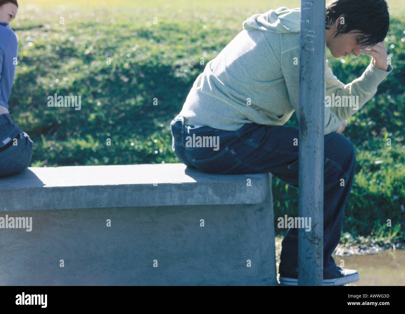 Teenage boy sitting on bench, his back turned to his friend holding his head, partial view Stock Photo