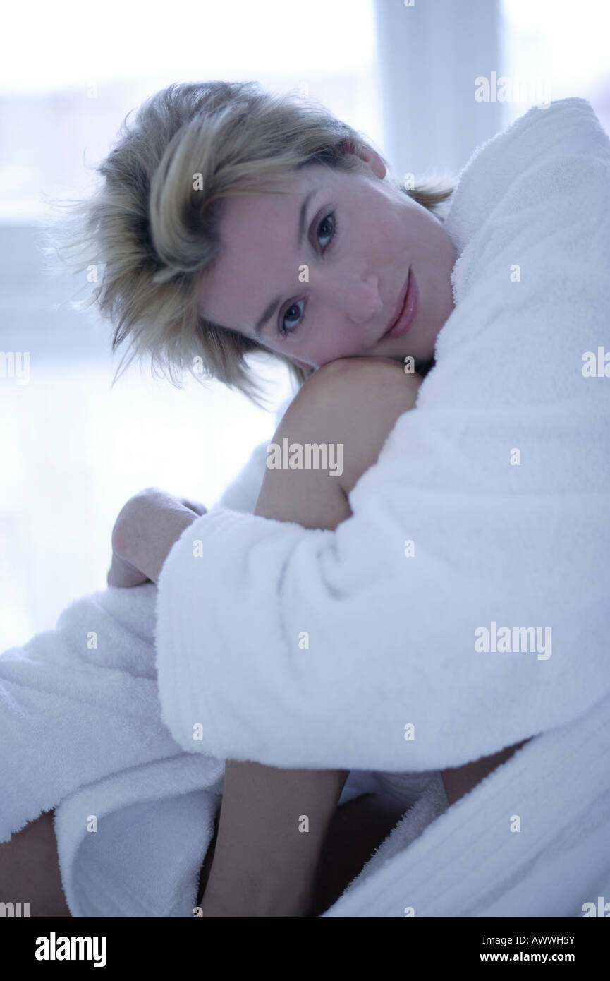 A woman sitting on the edge of a bed hugging her knees, close up Stock ...
