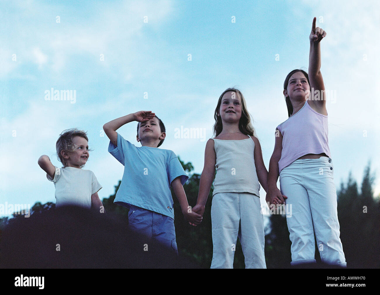 Children holding hands outdoors, one pointing, one shielding eyes, front view Stock Photo