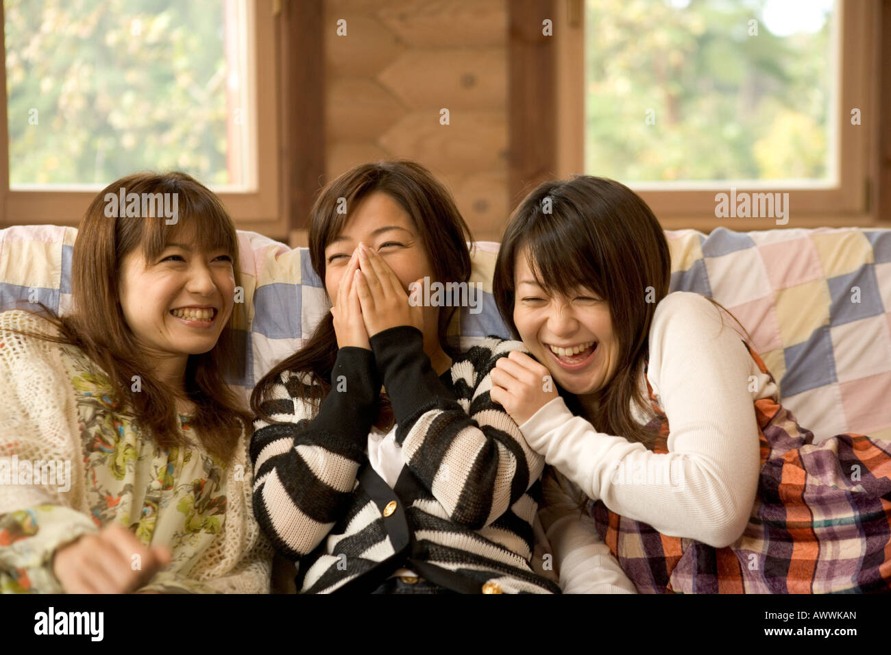 Three young women sitting on sofa and laughing Stock Photo - Alamy