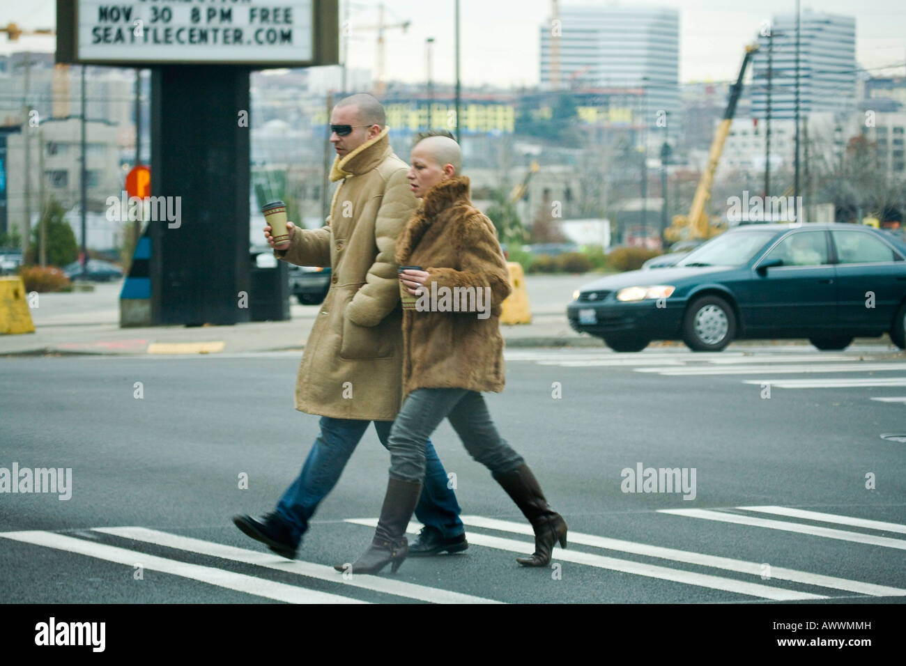 couple in letaher jackets and shaved heads walking in seattle with coffee in hand Stock Photo