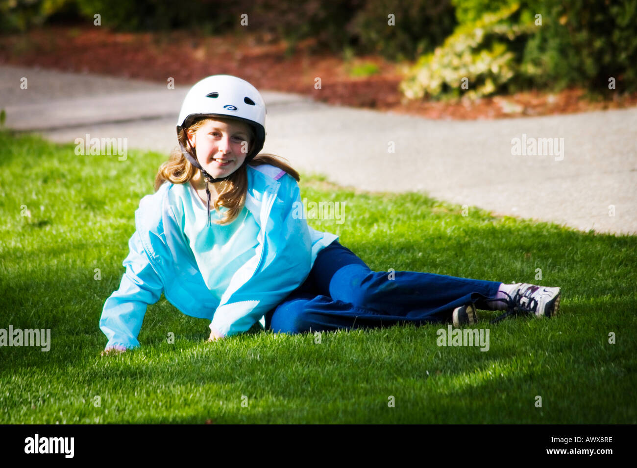 young girl sitting in the grass on a sunny spring late afternoon wearing a bicycle helmet smiling at the camera Stock Photo