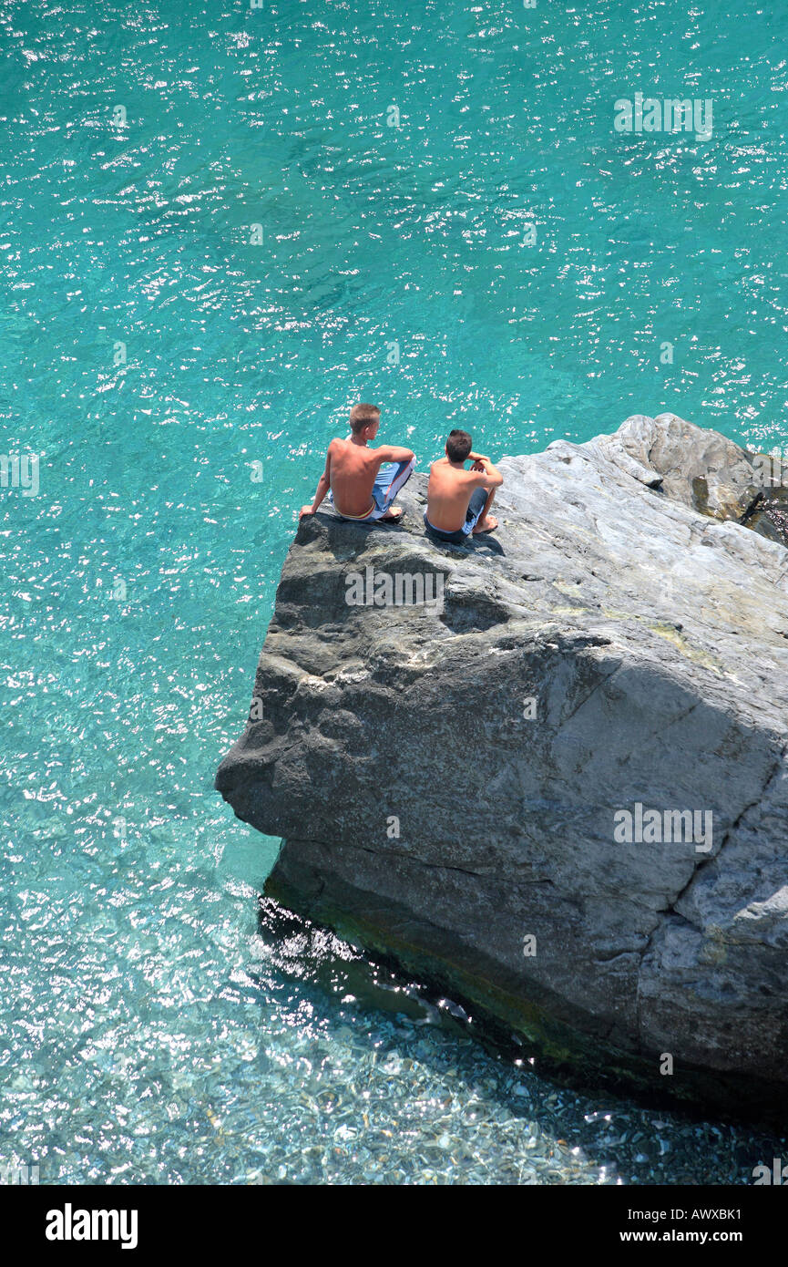 Aerial photo of two young boys sitting on rock looking into deep blue ...