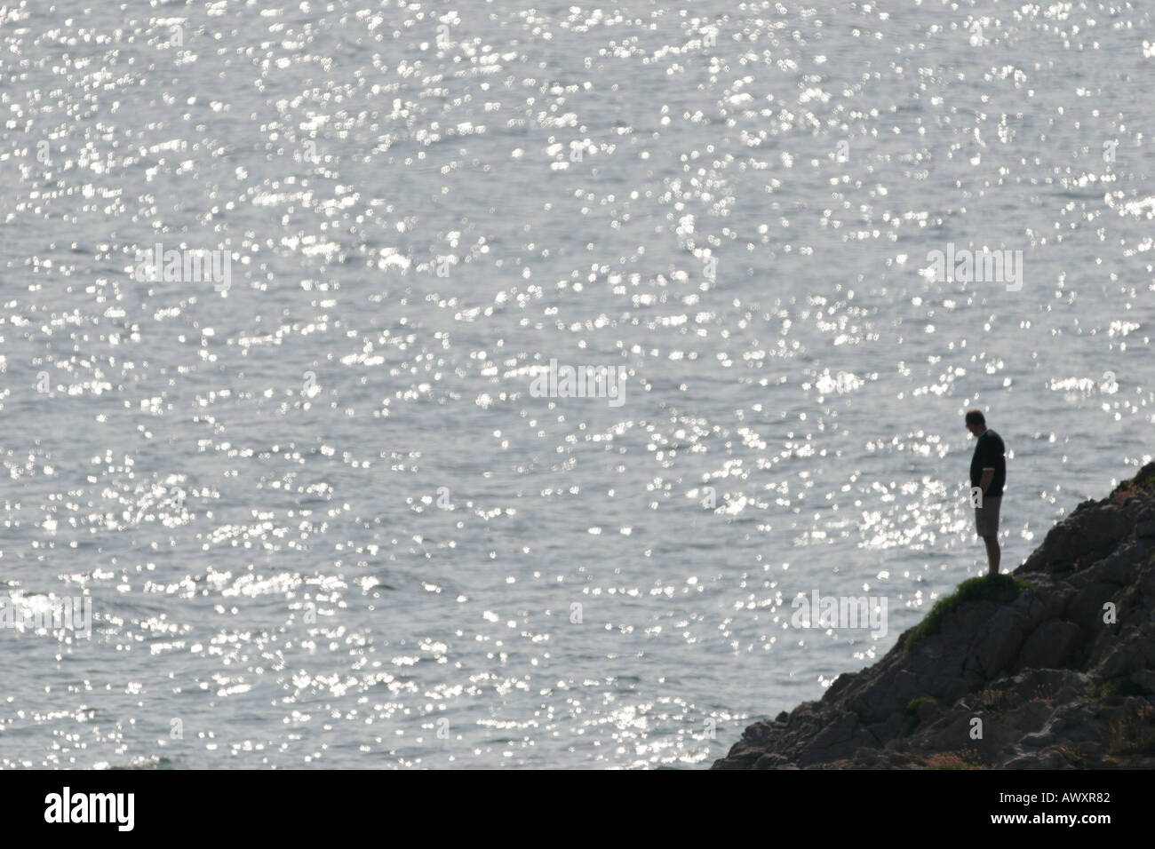 SILHOUETTE OF A MAN STANDING ON ROCKS BY THE OCEAN Stock Photo