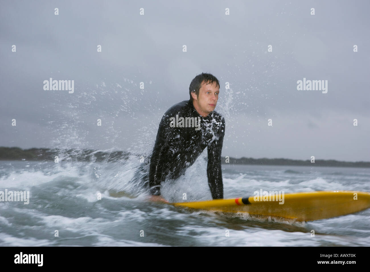 Surfer pulling himself up onto surfboard in water Stock Photo