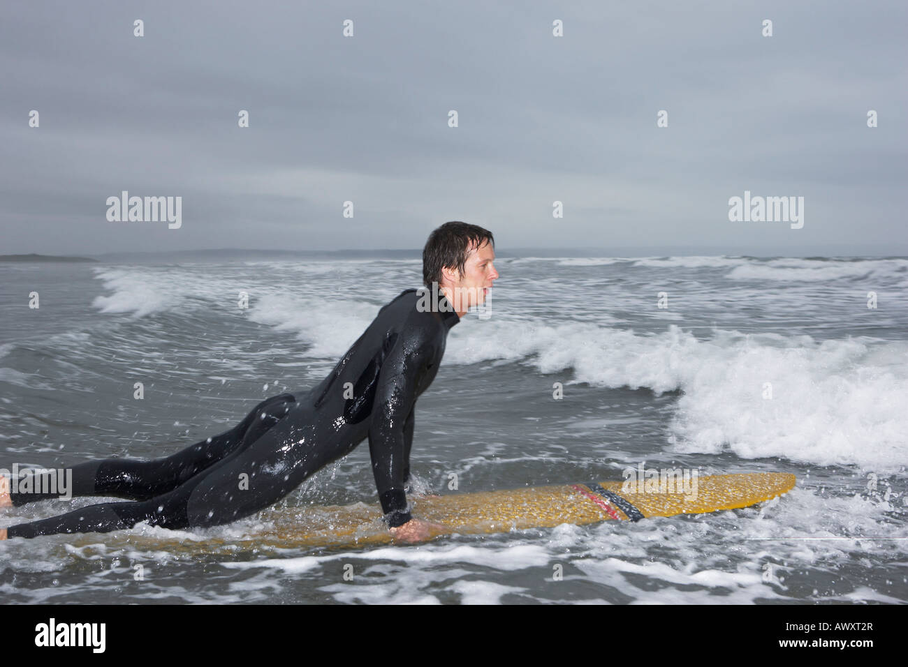 Surfer pulling himself up onto surfboard in water, side view Stock Photo