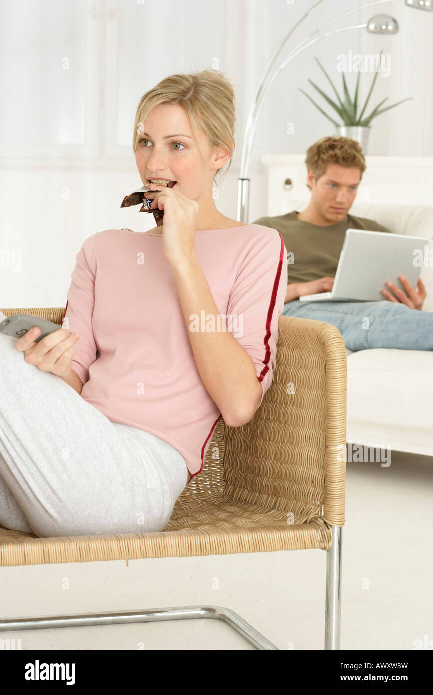 Woman Sitting On Chair Eating Candy Bar And Looking Tv Man