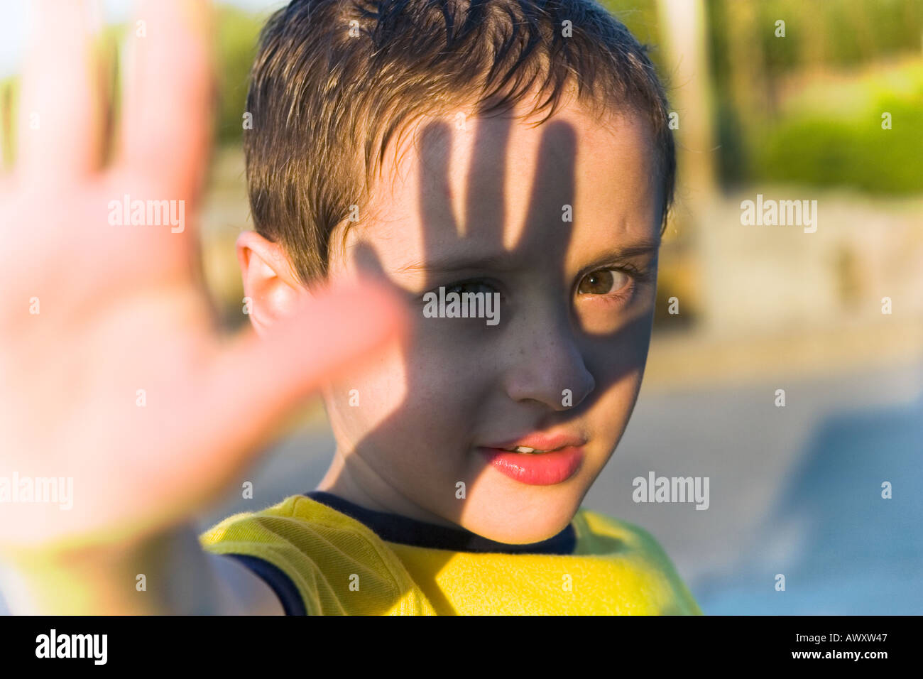 Young boy blocking sunlight with his hand causing a handprint shadow upon his face Stock Photo
