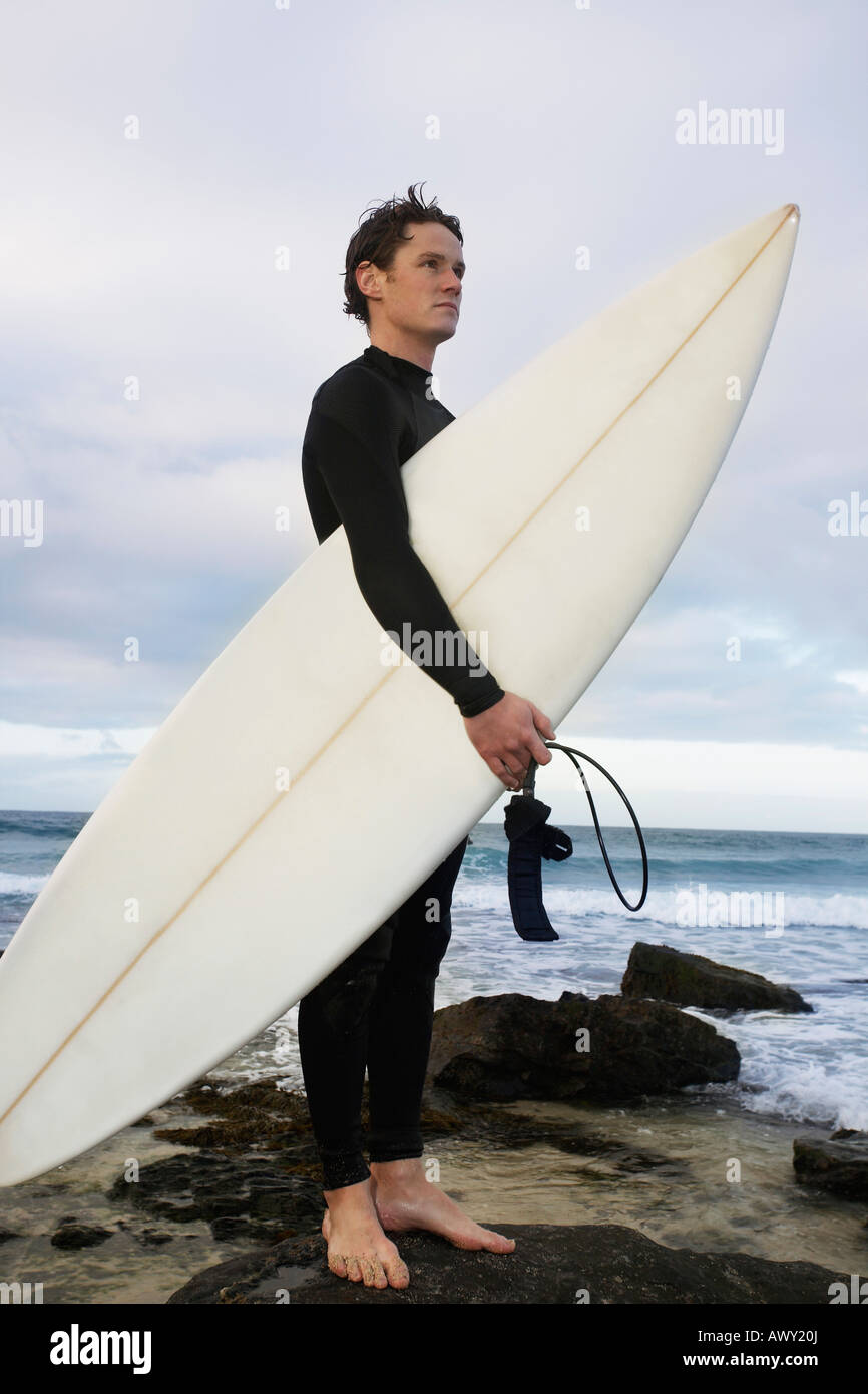 Man holding surfboard on rocks on beach, side view Stock Photo Alamy
