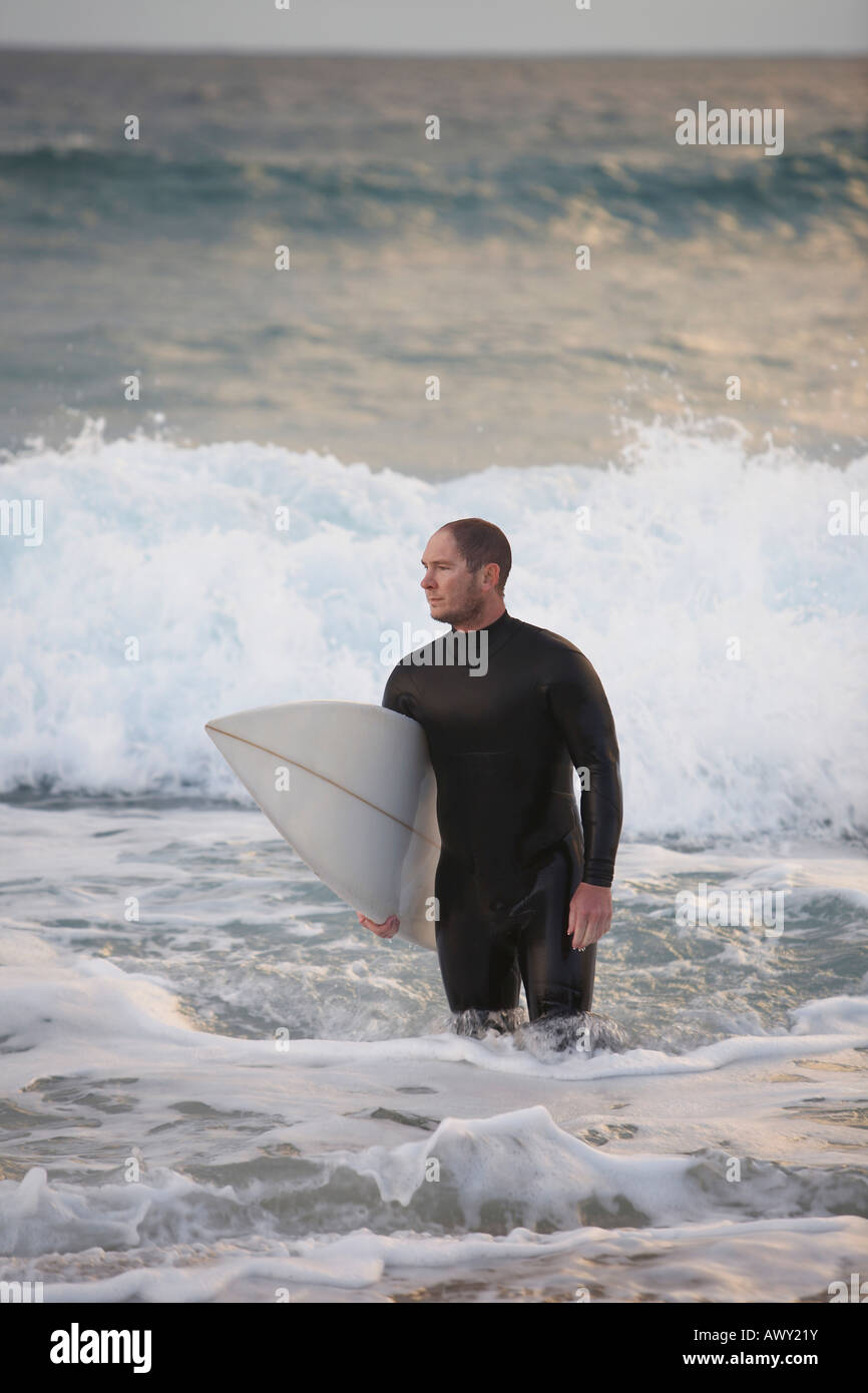 Surfer carrying surfboard out from sea Stock Photo