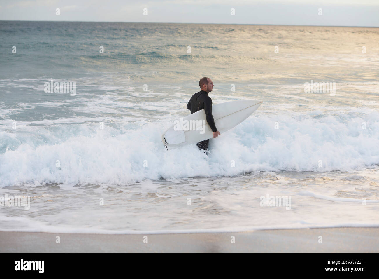 Surfer carrying surfboard in sea, side view Stock Photo