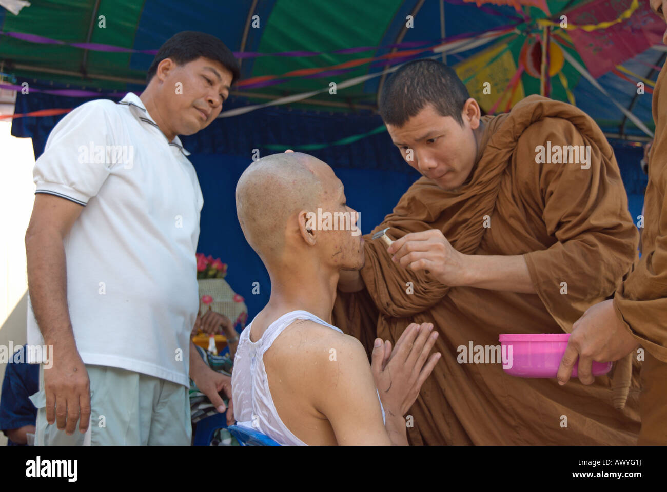 a thai buddhist monk shaves the chin of a young thai man, part of the ordination of a novice