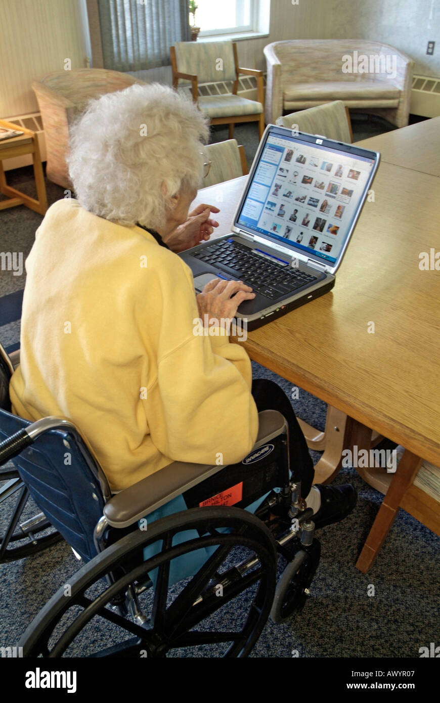 Handicapped Senior female in a wheelchair in a nursing home checks email on a wireless internet connection on a laptop computer Stock Photo