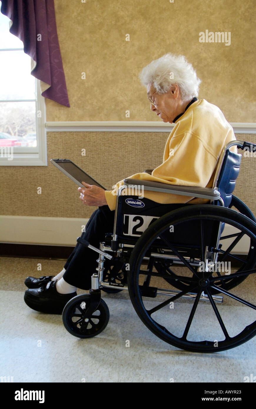 Handicapped Senior female in a wheelchair in a nursing home checks email on a wireless internet connection on a laptop computer Stock Photo