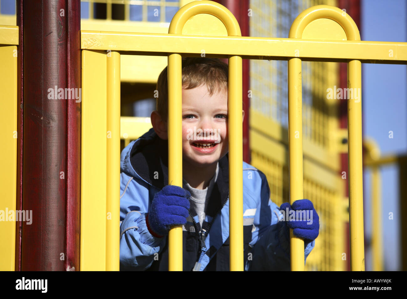 Young boy a park looking through yellow bars Stock Photo