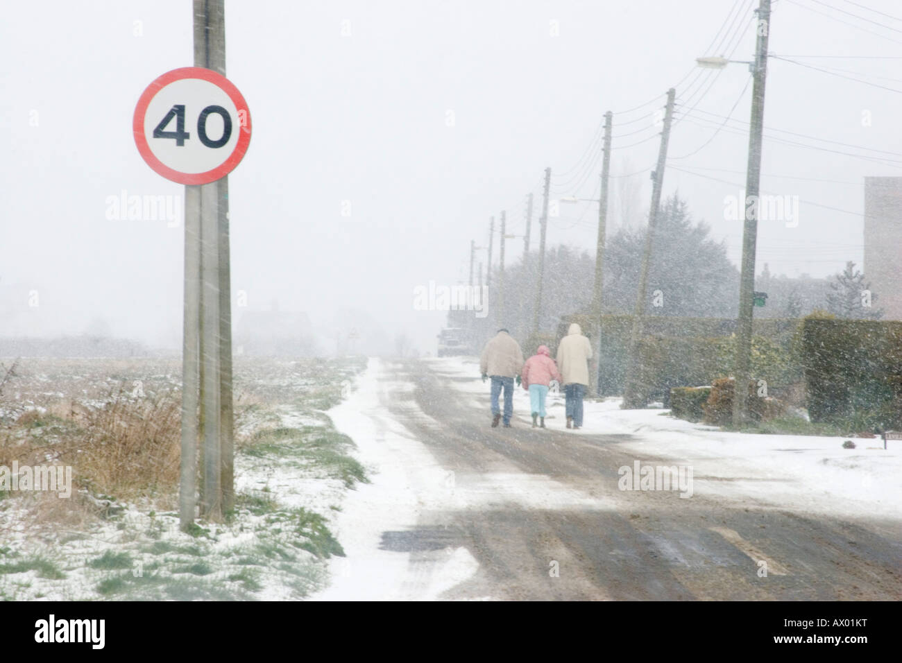 Three people walking down a road in the snow in winter, with a 40 miles per hour sign in the foreground Stock Photo